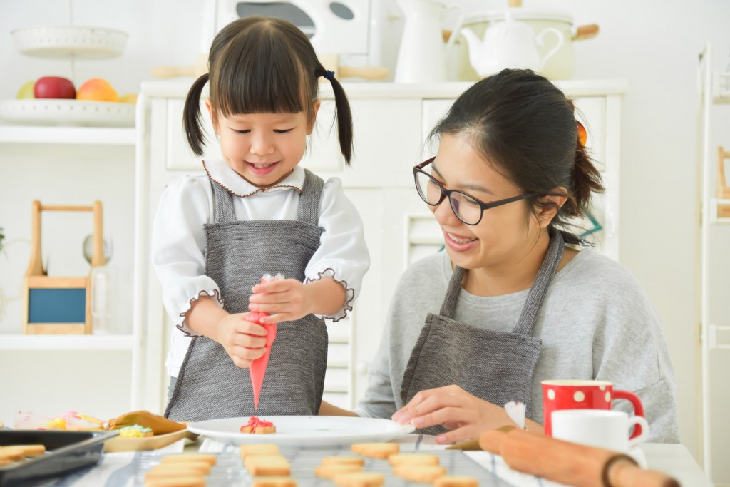 Asian Kid and young mother decorating cookies.