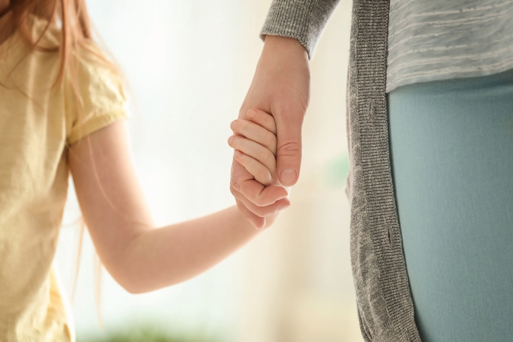 Mother and her little daughter holding hands on blurred backgrou